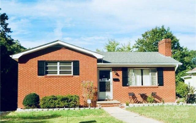 view of front facade with a front yard, brick siding, and a chimney