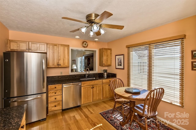 kitchen featuring stainless steel appliances, a ceiling fan, a sink, dark stone countertops, and light wood-type flooring