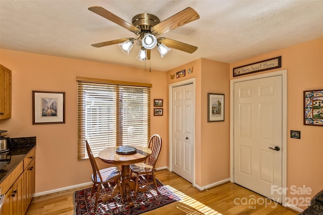 dining room featuring a textured ceiling, ceiling fan, light wood finished floors, and baseboards