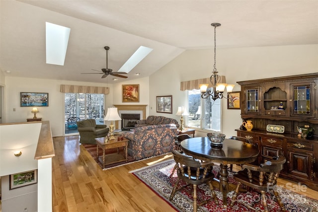 dining area featuring light wood-type flooring, vaulted ceiling with skylight, plenty of natural light, and a fireplace