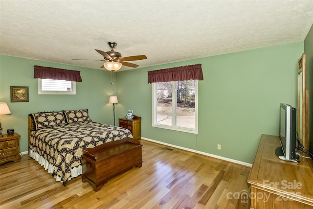 bedroom featuring ceiling fan, light wood-style flooring, baseboards, and a textured ceiling