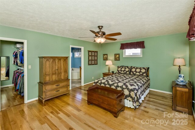 bedroom featuring light wood finished floors, baseboards, a walk in closet, and a closet