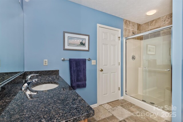 full bath featuring a stall shower, baseboards, stone finish floor, a textured ceiling, and a sink