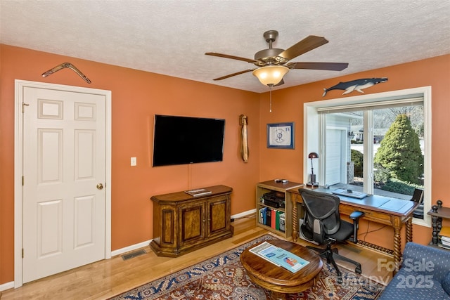 office featuring a textured ceiling, a ceiling fan, visible vents, and light wood-style floors