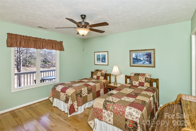 bedroom featuring visible vents, baseboards, ceiling fan, wood finished floors, and a textured ceiling