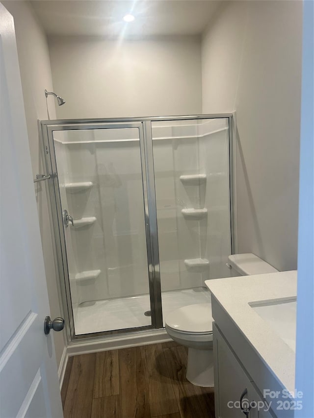 bathroom with toilet, a shower stall, wood finished floors, and vanity