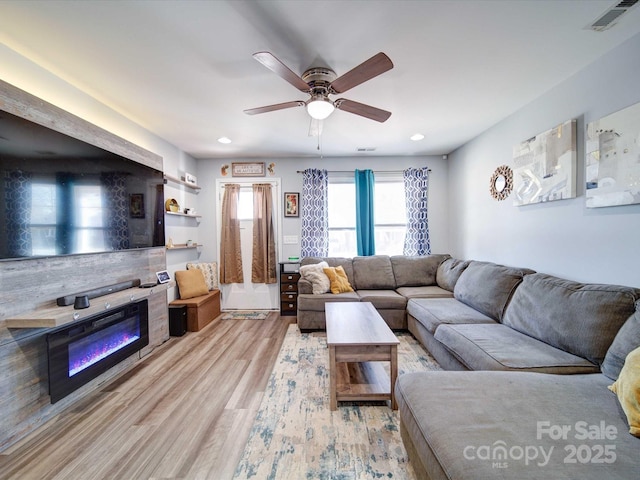 living area with ceiling fan, light wood-style flooring, recessed lighting, visible vents, and a glass covered fireplace