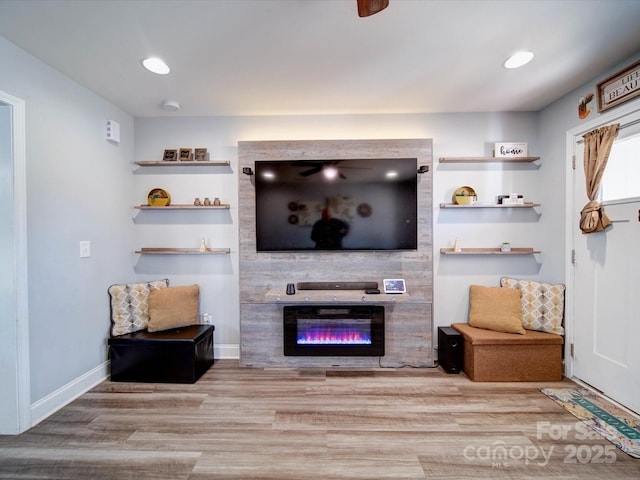 living area with light wood finished floors, recessed lighting, a glass covered fireplace, and baseboards