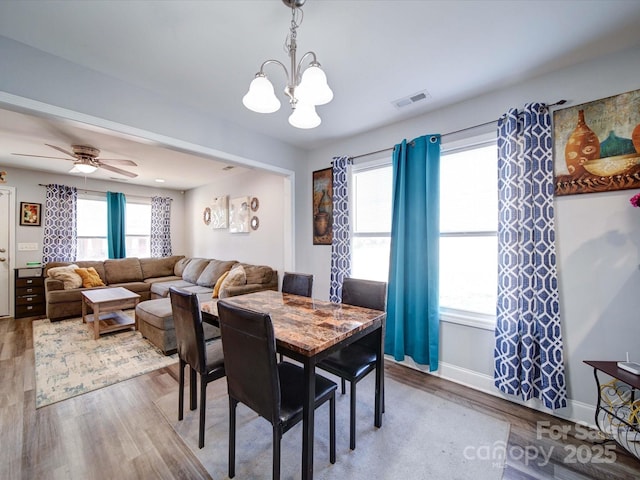 dining area featuring ceiling fan with notable chandelier, wood finished floors, visible vents, and baseboards