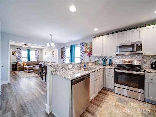 kitchen with appliances with stainless steel finishes, open floor plan, a peninsula, white cabinetry, and a sink