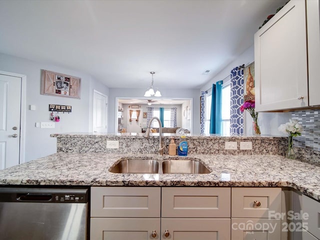 kitchen featuring light stone counters, decorative light fixtures, white cabinets, a sink, and dishwasher