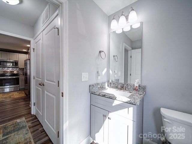 bathroom with tasteful backsplash, toilet, wood finished floors, vanity, and a closet