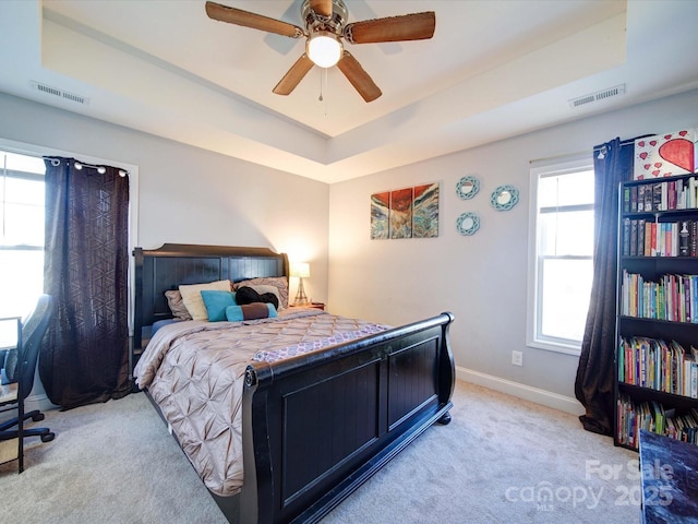 bedroom with a tray ceiling, visible vents, and carpet flooring