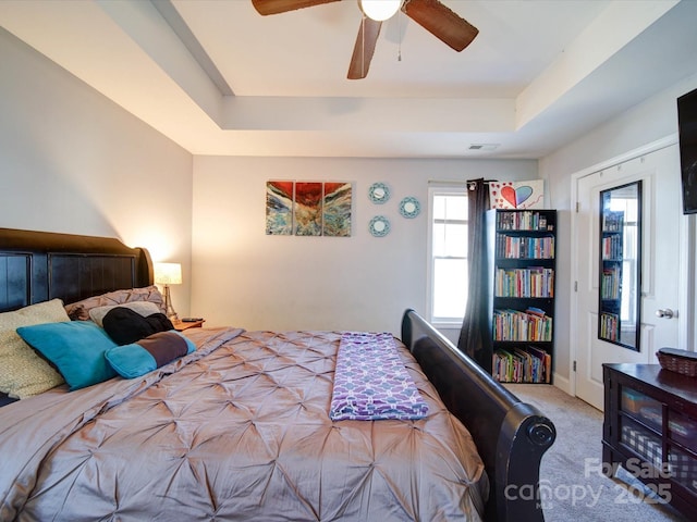 bedroom with a ceiling fan, visible vents, a tray ceiling, and carpet flooring