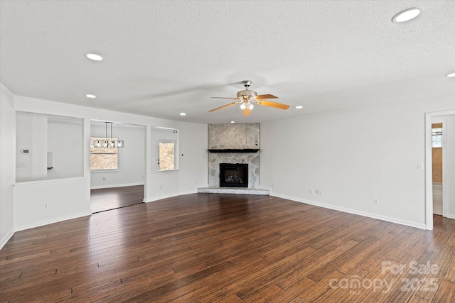 unfurnished living room with dark wood-type flooring, a large fireplace, a textured ceiling, and a ceiling fan