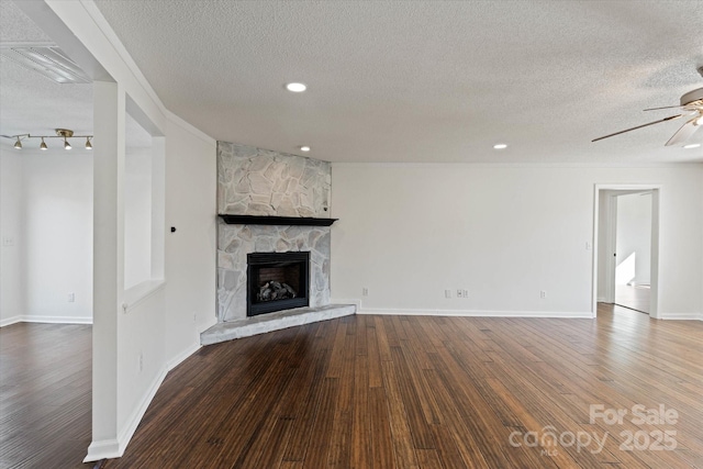 unfurnished living room with ceiling fan, a stone fireplace, a textured ceiling, and hardwood / wood-style flooring