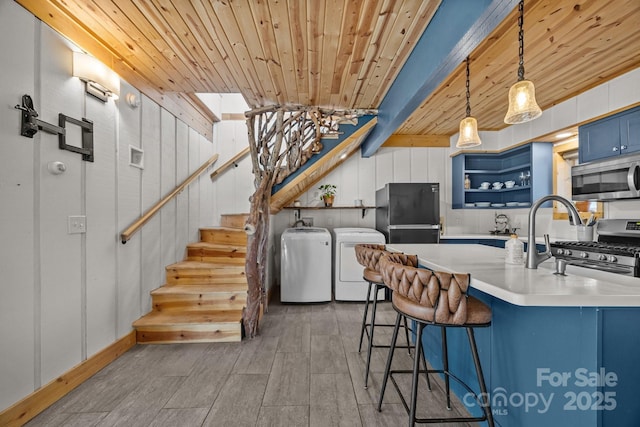 kitchen featuring blue cabinetry, open shelves, hanging light fixtures, appliances with stainless steel finishes, and washing machine and dryer