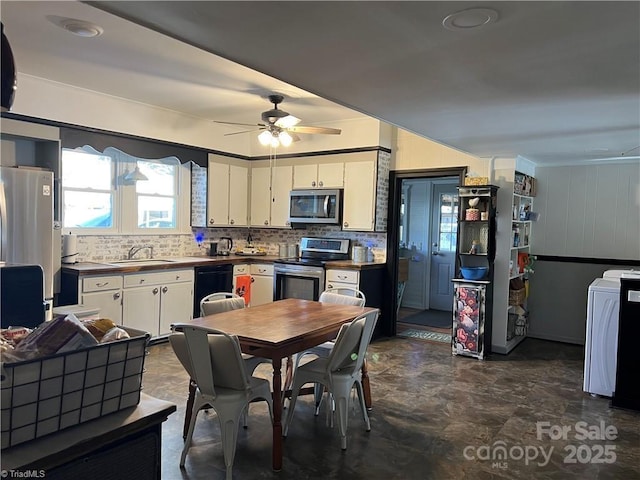 kitchen with stainless steel appliances, a sink, white cabinetry, dark countertops, and washer / dryer