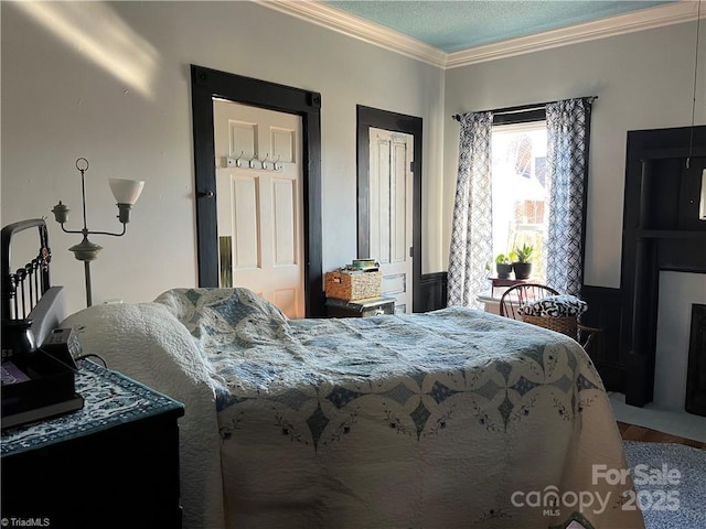 bedroom featuring a textured ceiling, crown molding, and wainscoting