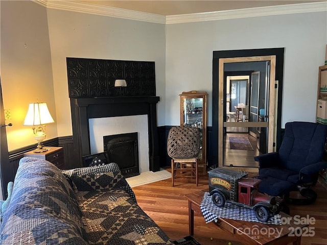 living area featuring wainscoting, a fireplace, crown molding, and wood finished floors