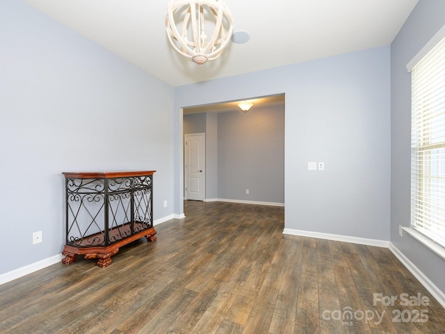 unfurnished room featuring wood finished floors, baseboards, and a chandelier