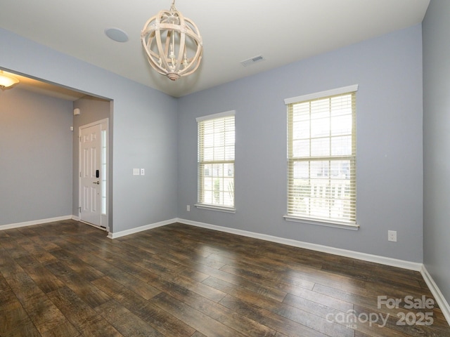 spare room featuring visible vents, baseboards, a notable chandelier, and dark wood finished floors