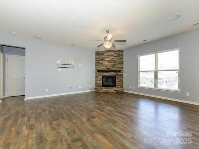 unfurnished living room with baseboards, dark wood-type flooring, a stone fireplace, and ceiling fan