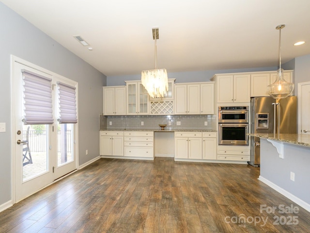 kitchen featuring backsplash, appliances with stainless steel finishes, glass insert cabinets, light stone countertops, and dark wood-style flooring