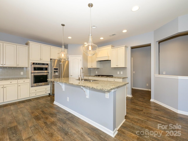 kitchen featuring a sink, dark wood-type flooring, light stone countertops, custom range hood, and a kitchen island with sink