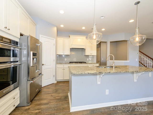 kitchen featuring dark wood-type flooring, premium range hood, a breakfast bar area, stainless steel appliances, and a sink