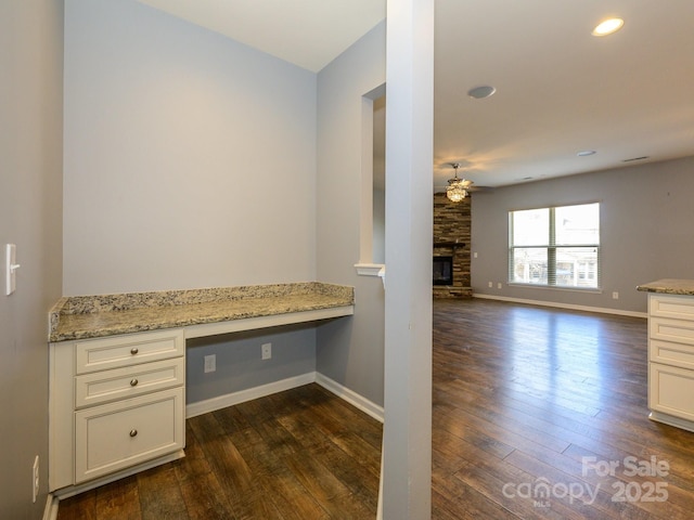 unfurnished office featuring dark wood finished floors, a fireplace, built in desk, and baseboards