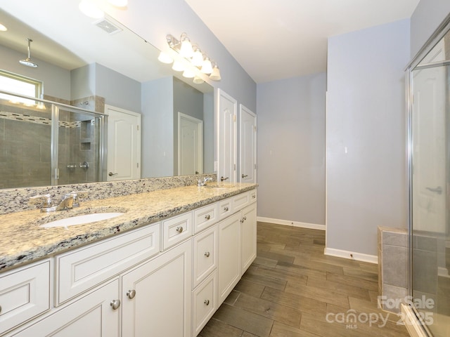 full bathroom with a sink, wood finished floors, a stall shower, and double vanity