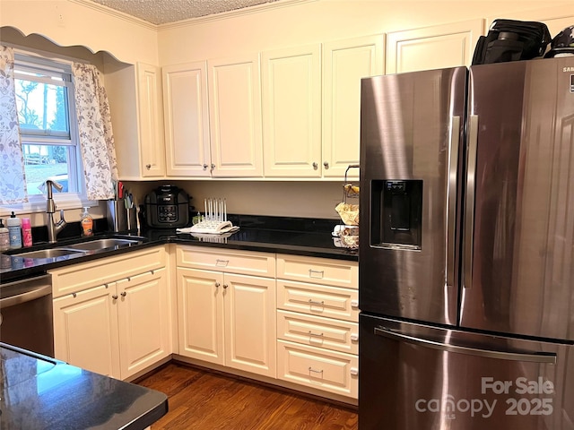 kitchen featuring appliances with stainless steel finishes, dark countertops, dark wood-type flooring, and a sink