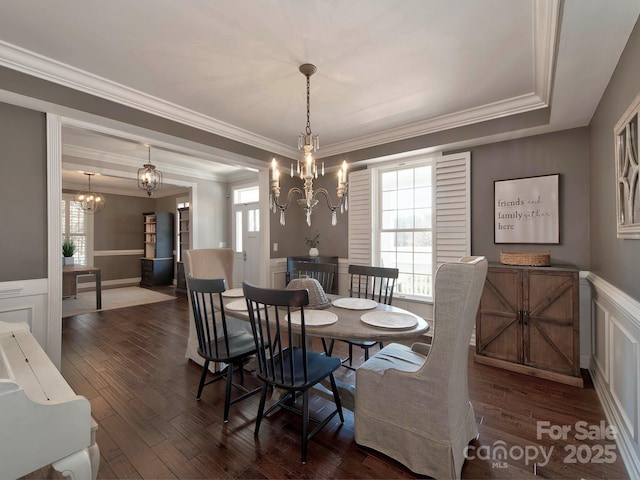 dining area with wainscoting, ornamental molding, dark wood-style flooring, a decorative wall, and a notable chandelier