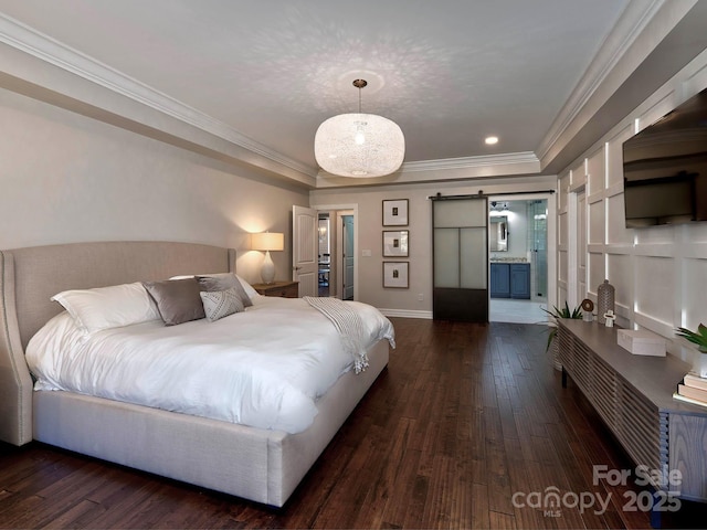 bedroom with a barn door, baseboards, connected bathroom, ornamental molding, and dark wood-style flooring