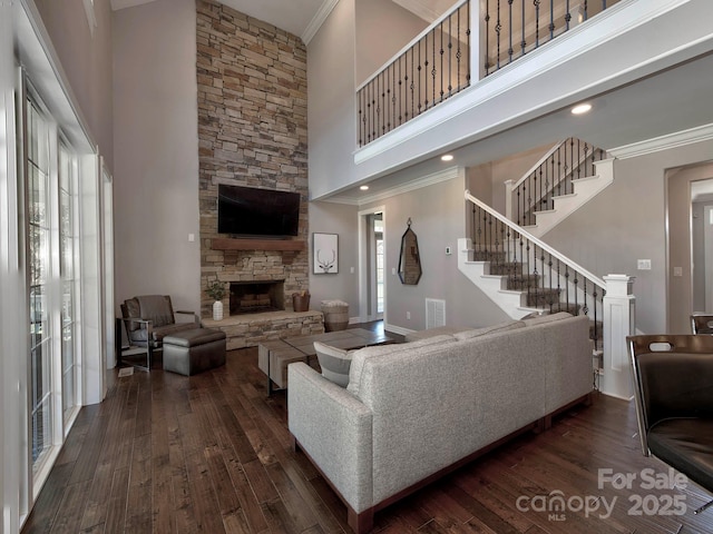 living area featuring dark wood-type flooring, visible vents, crown molding, and a stone fireplace