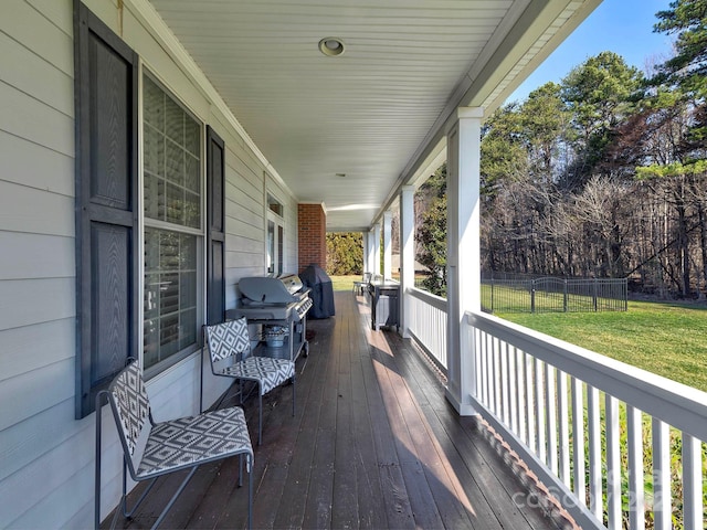 wooden terrace featuring covered porch, a grill, a lawn, and fence