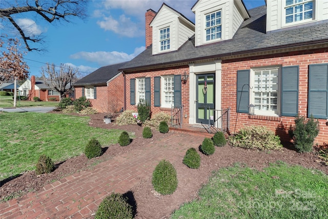 view of front of home with a shingled roof, a front yard, and brick siding