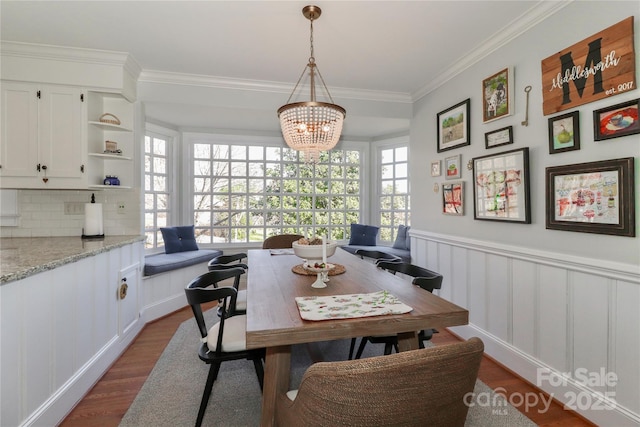 dining space with dark wood-style floors, a notable chandelier, crown molding, a decorative wall, and wainscoting