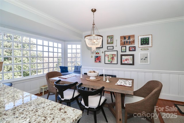 dining area with a wainscoted wall, an inviting chandelier, crown molding, and wood finished floors