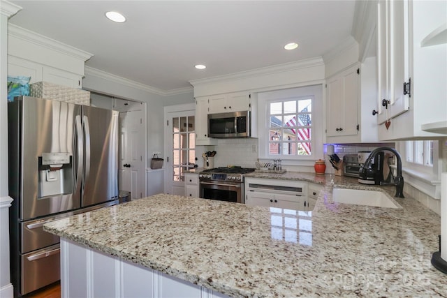 kitchen featuring crown molding, appliances with stainless steel finishes, white cabinetry, a sink, and a peninsula