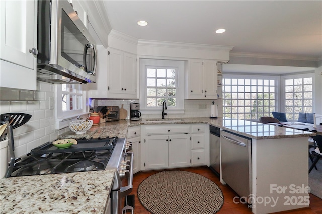 kitchen with crown molding, appliances with stainless steel finishes, white cabinetry, a sink, and a peninsula