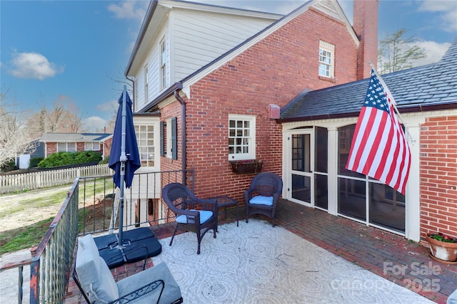 rear view of house featuring brick siding, fence, and a sunroom