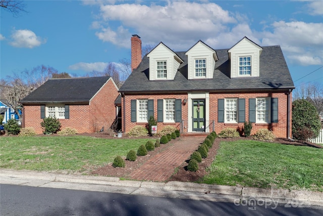 new england style home with brick siding, a chimney, and a front lawn