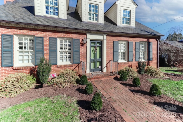 entrance to property featuring roof with shingles and brick siding