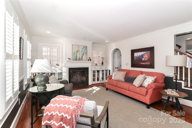 living room with arched walkways, stairway, ornamental molding, a fireplace with flush hearth, and wood finished floors