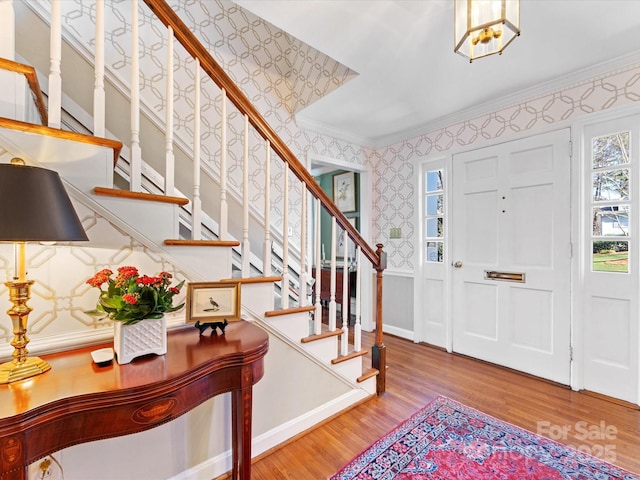 foyer entrance with stairs, ornamental molding, wood finished floors, and wallpapered walls