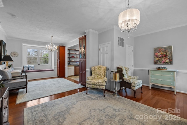 living area with visible vents, ornamental molding, hardwood / wood-style flooring, a textured ceiling, and a notable chandelier