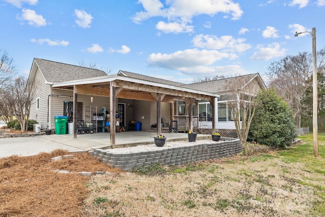 back of house featuring a carport, concrete driveway, and roof with shingles