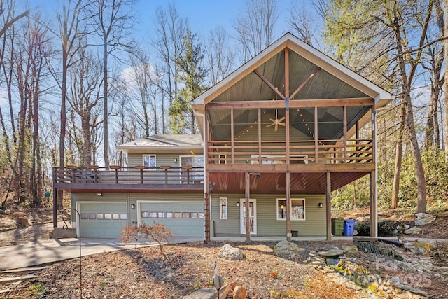 rustic home with a sunroom, concrete driveway, a wooden deck, and an attached garage